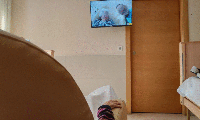 Persona mayor en residencia viendo fotos familiares en el televisor de su habitación