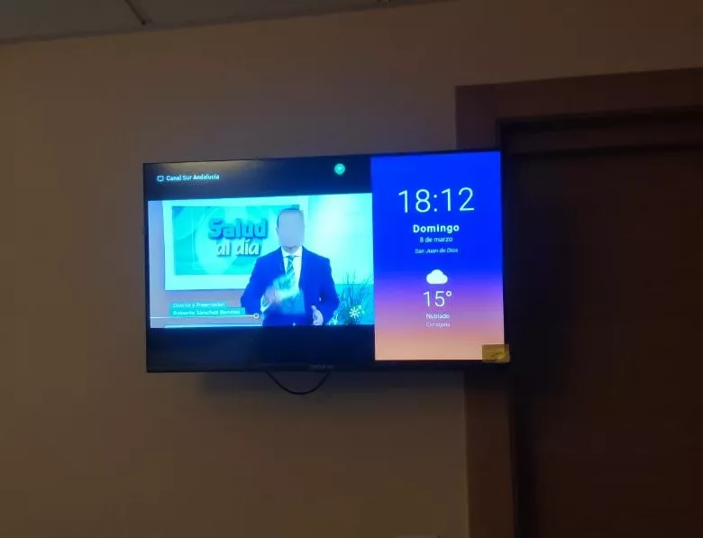 Televisor de habitación mostrando canal TDT con reloj, fecha y clima